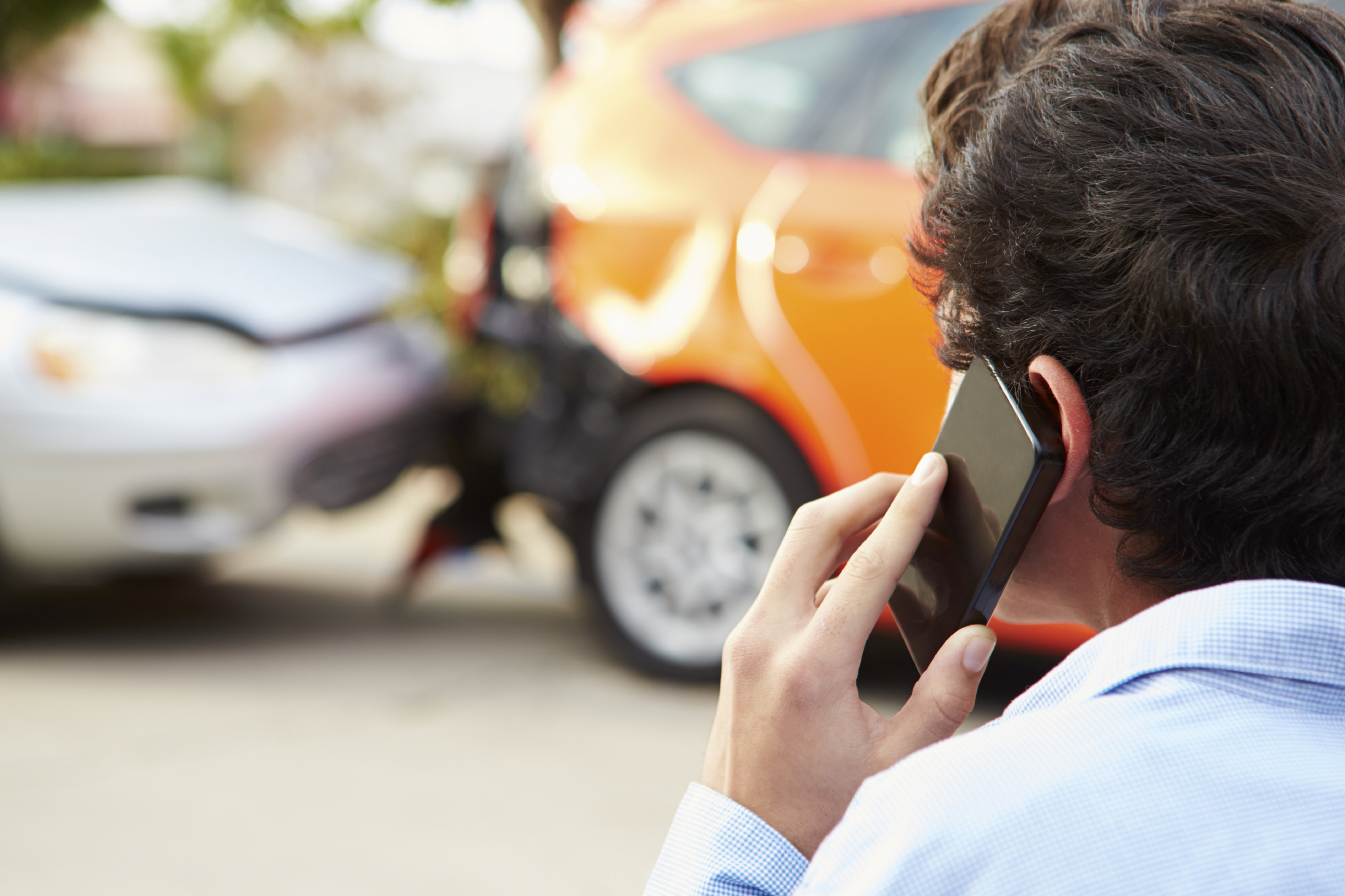Back of young man's head, holding a cellphone at the scene of a crash.