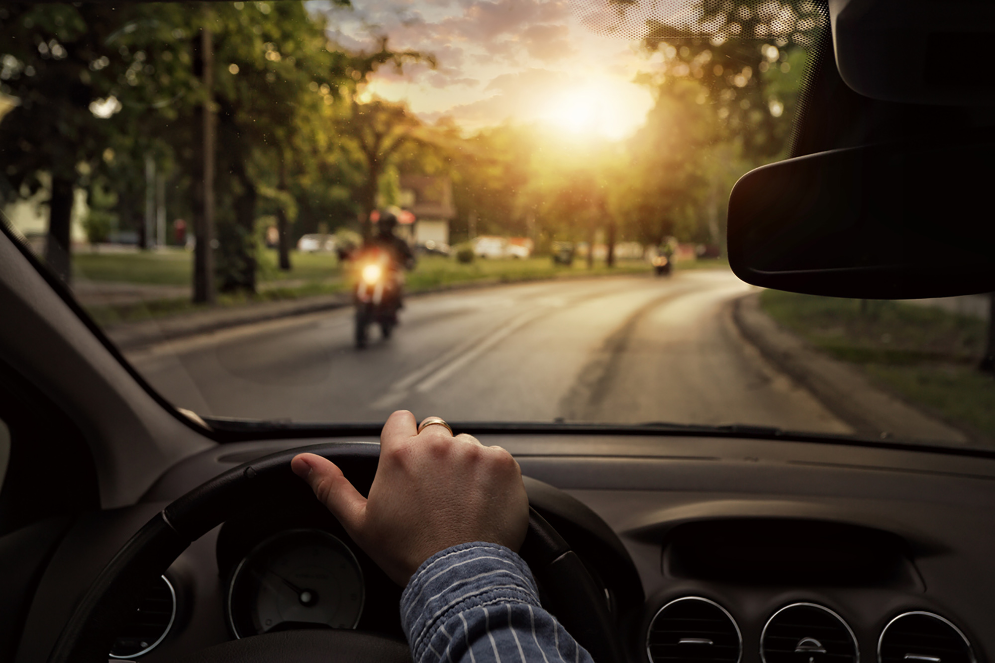 Driver with hands on wheel and a motorcycle in front of them on the road.