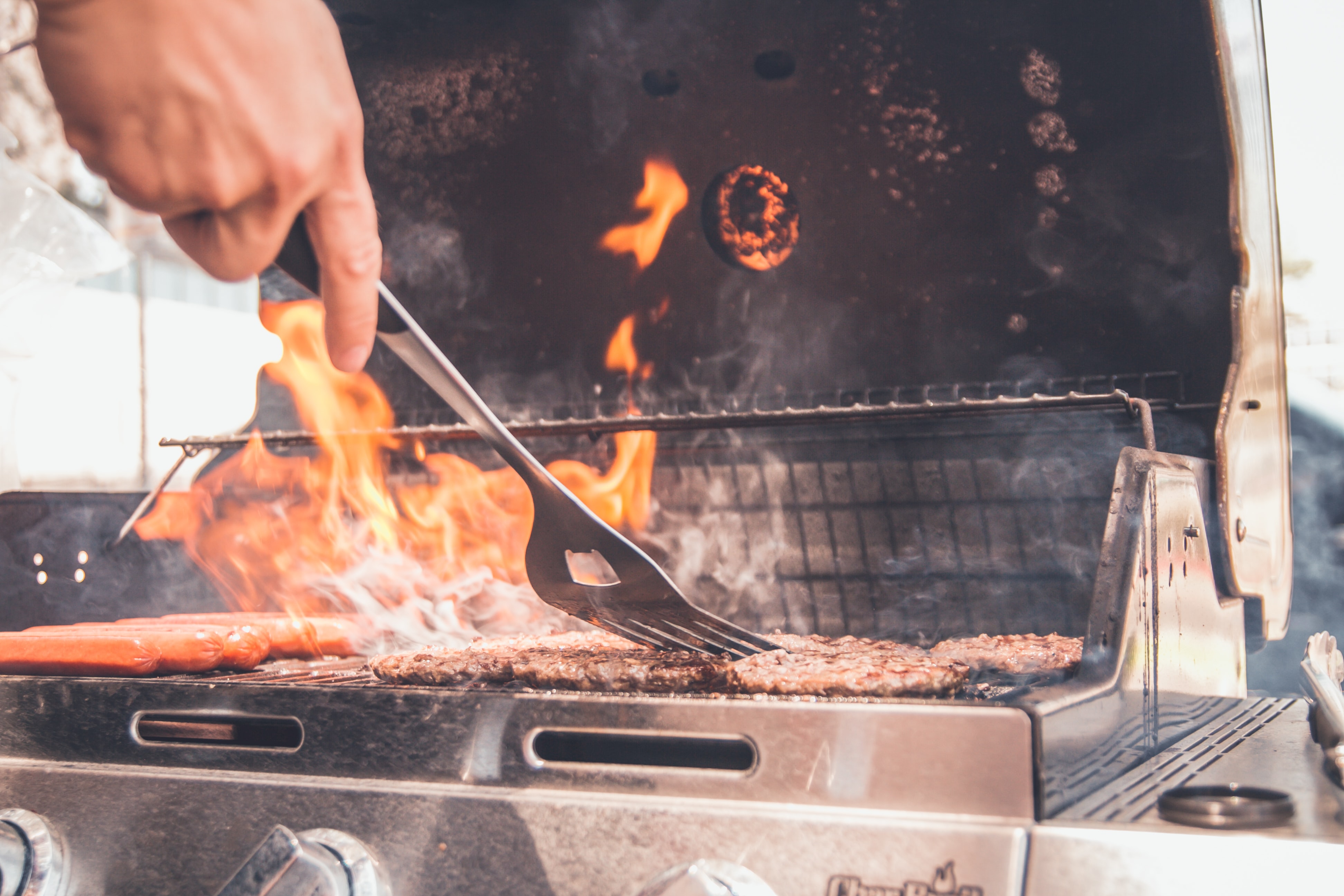 Close up of person grilling burgers and hotdogs on gas grill.
