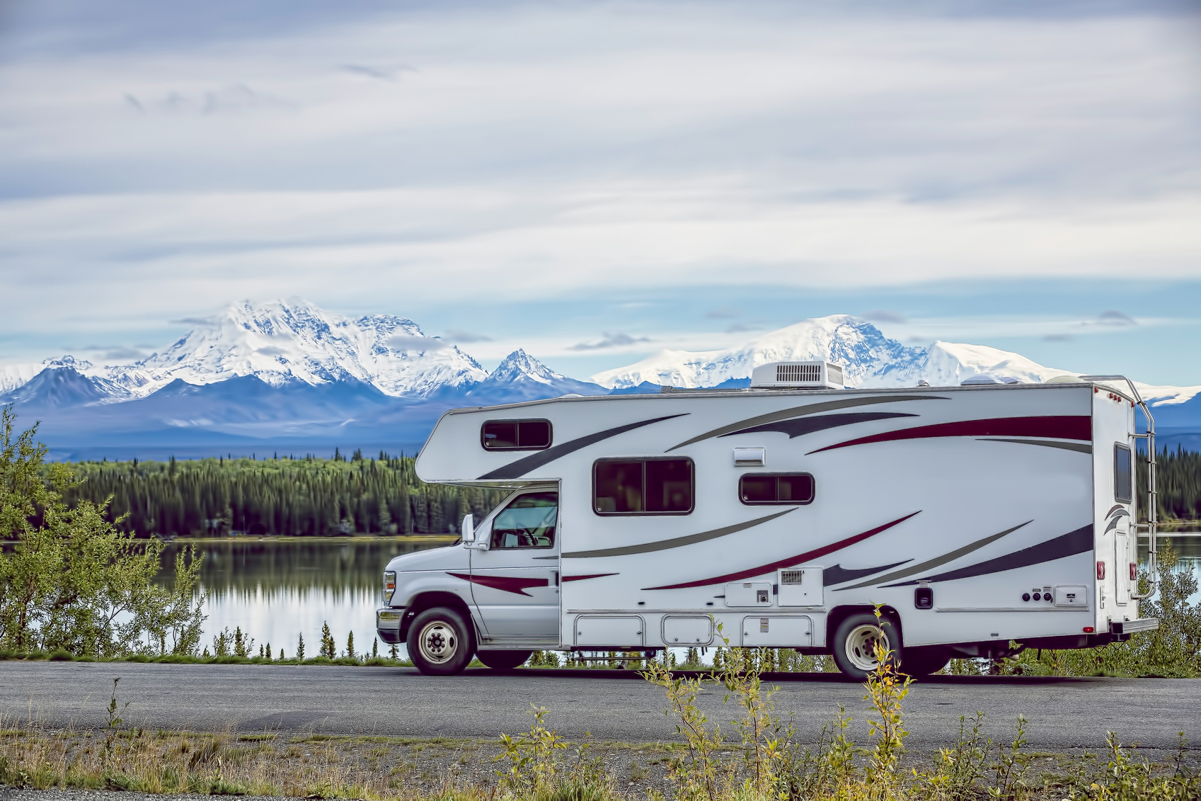 RV parked on rural Alaskan road with lake and mountains in the background.