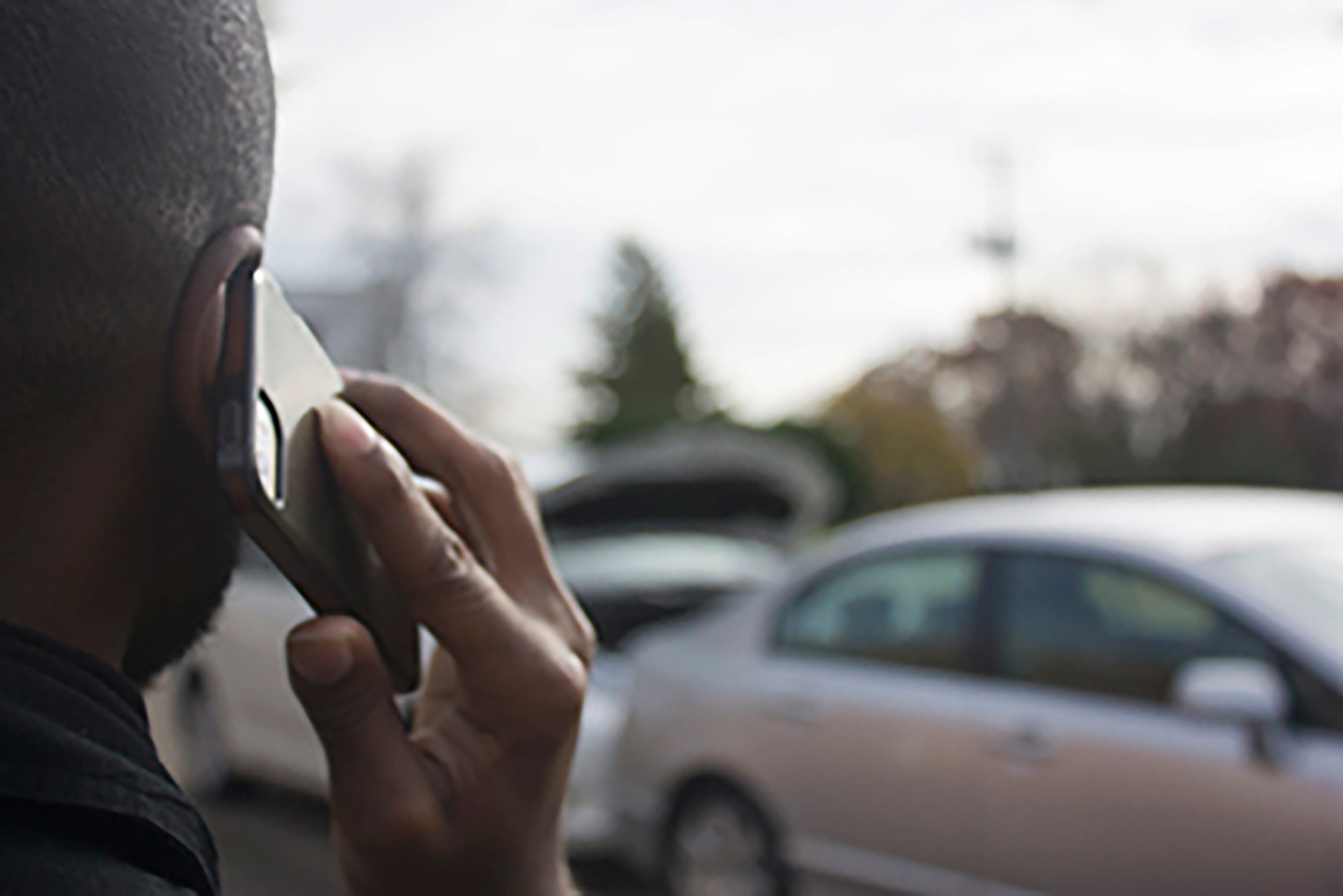 Person on the phone with two cars in the background.