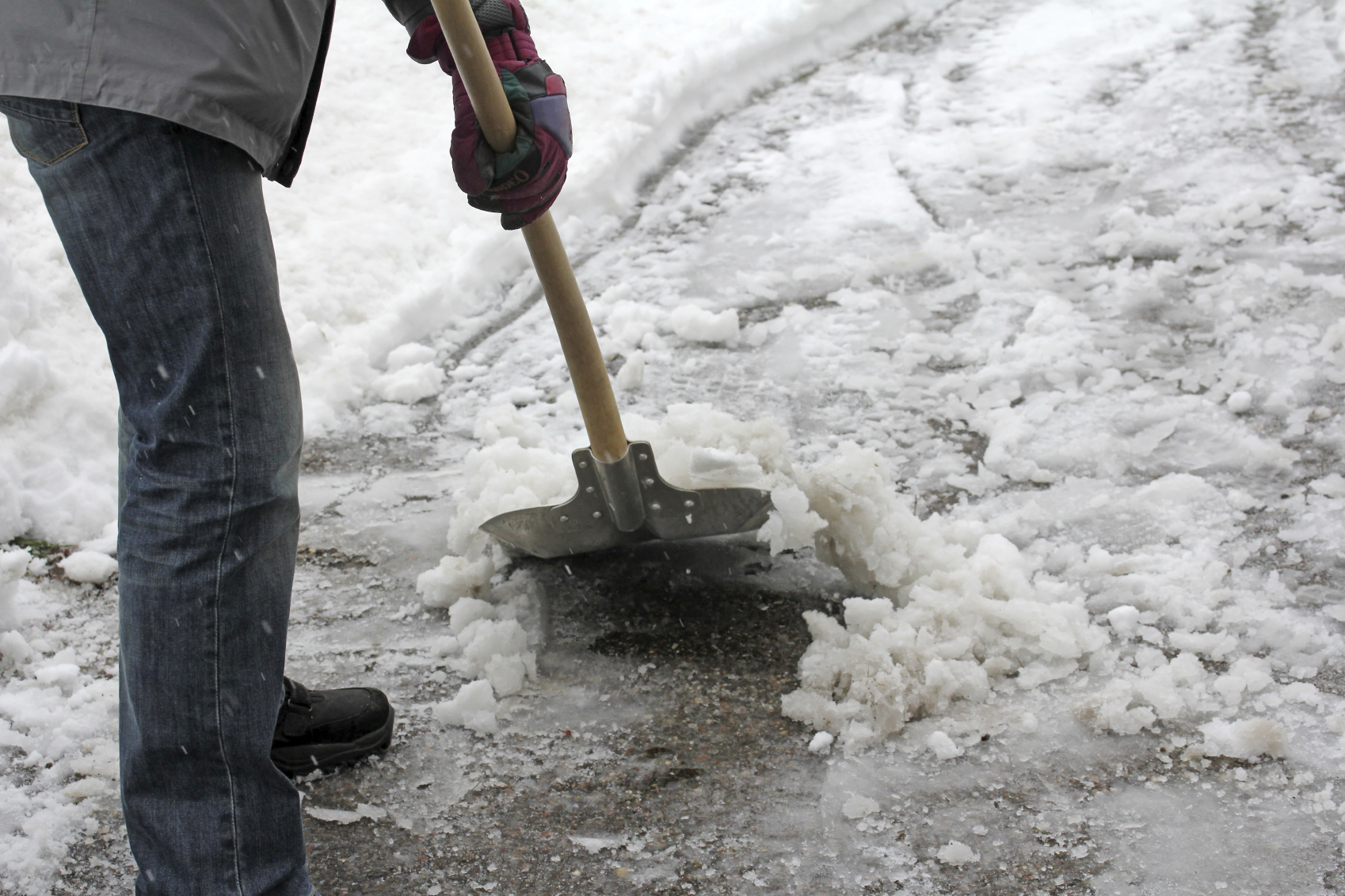 Individual scraping and shoveling ice from a driveway.