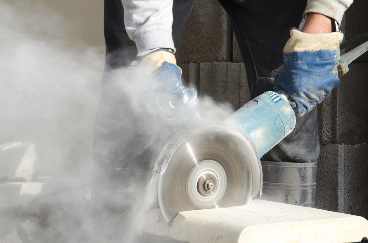 Person using a circular saw to cut stone-like material, producing a cloud of white dust.
