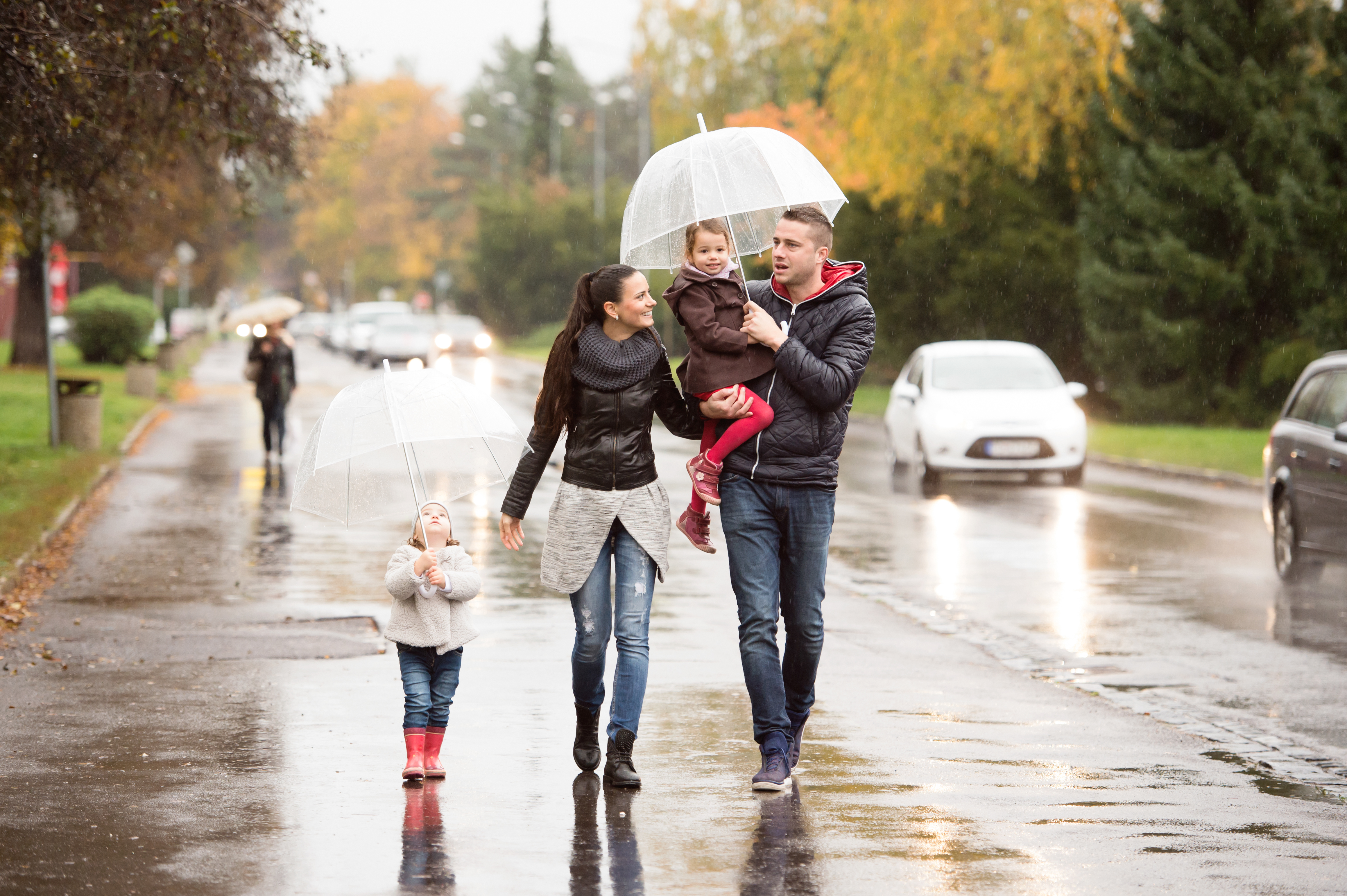 Young family of four walking down the street in the rain with an umbrella.