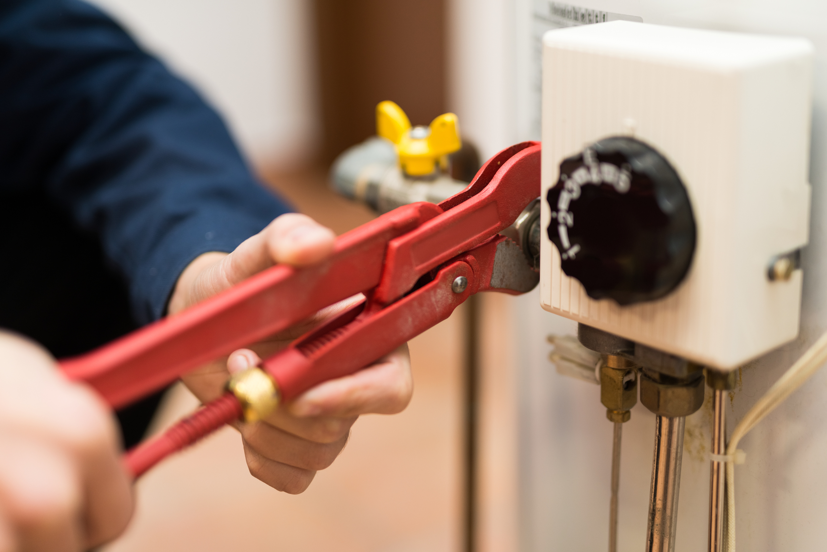Close-up of a person using a wrench to work on a water heater.