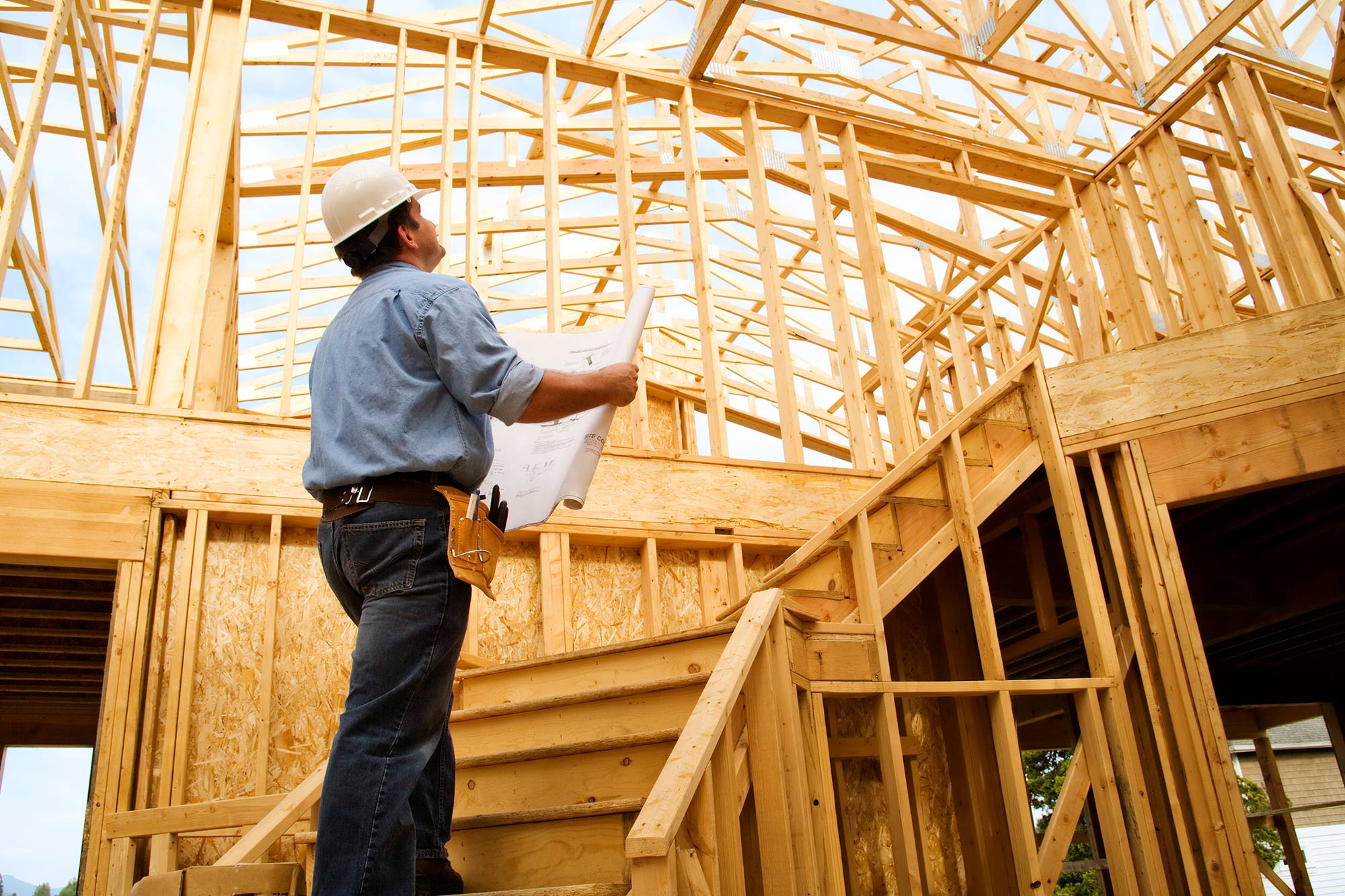 Contractor in hardhat examining building plans in wooden frame of house.