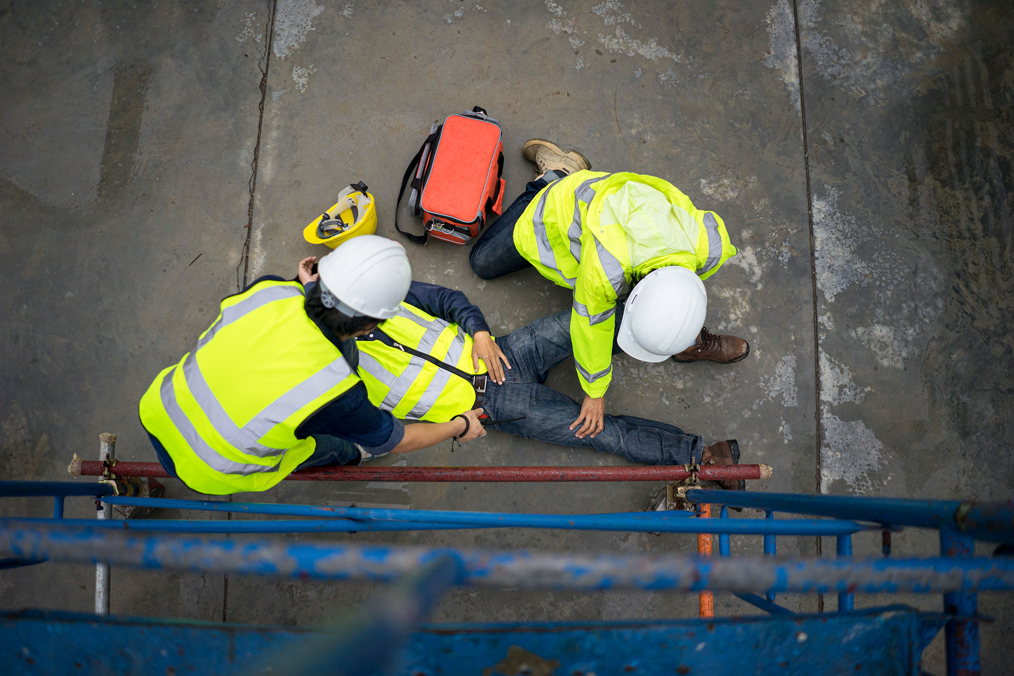 Two construction workers tending to an injured employee laying on the ground.