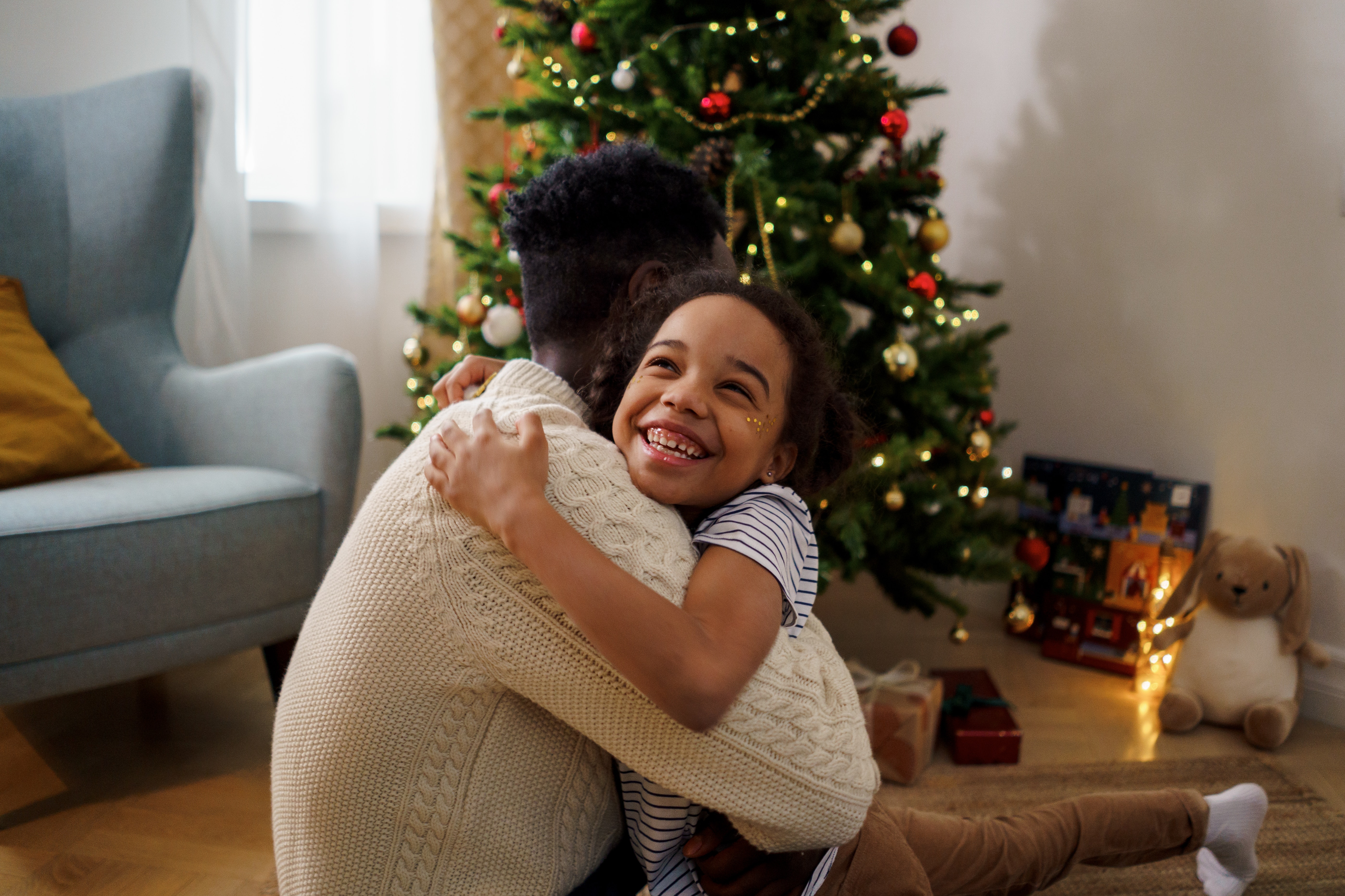Father and daughter hugging in front of a decorated holiday tree.