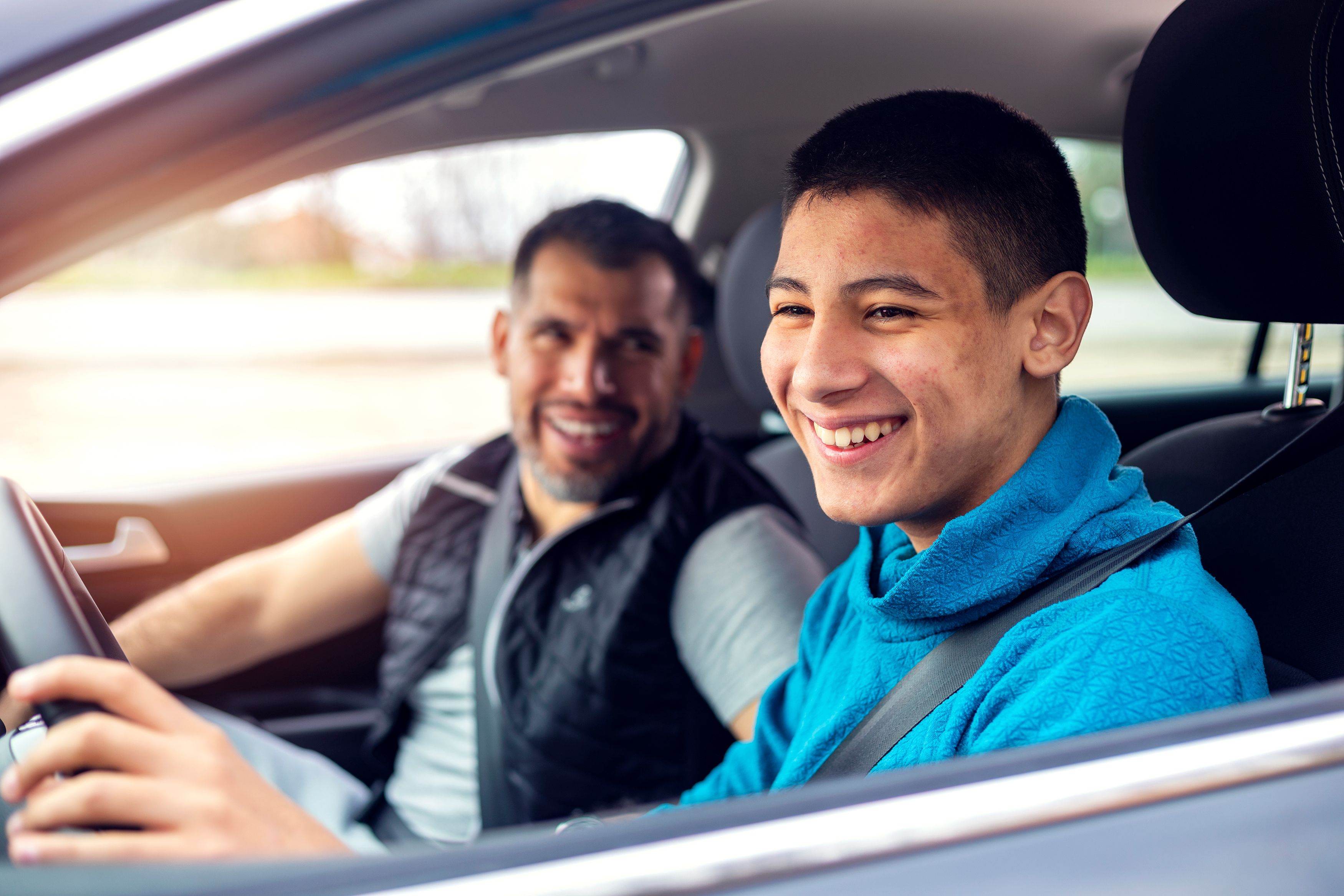 Teen boy driving car with father in the passenger seat.