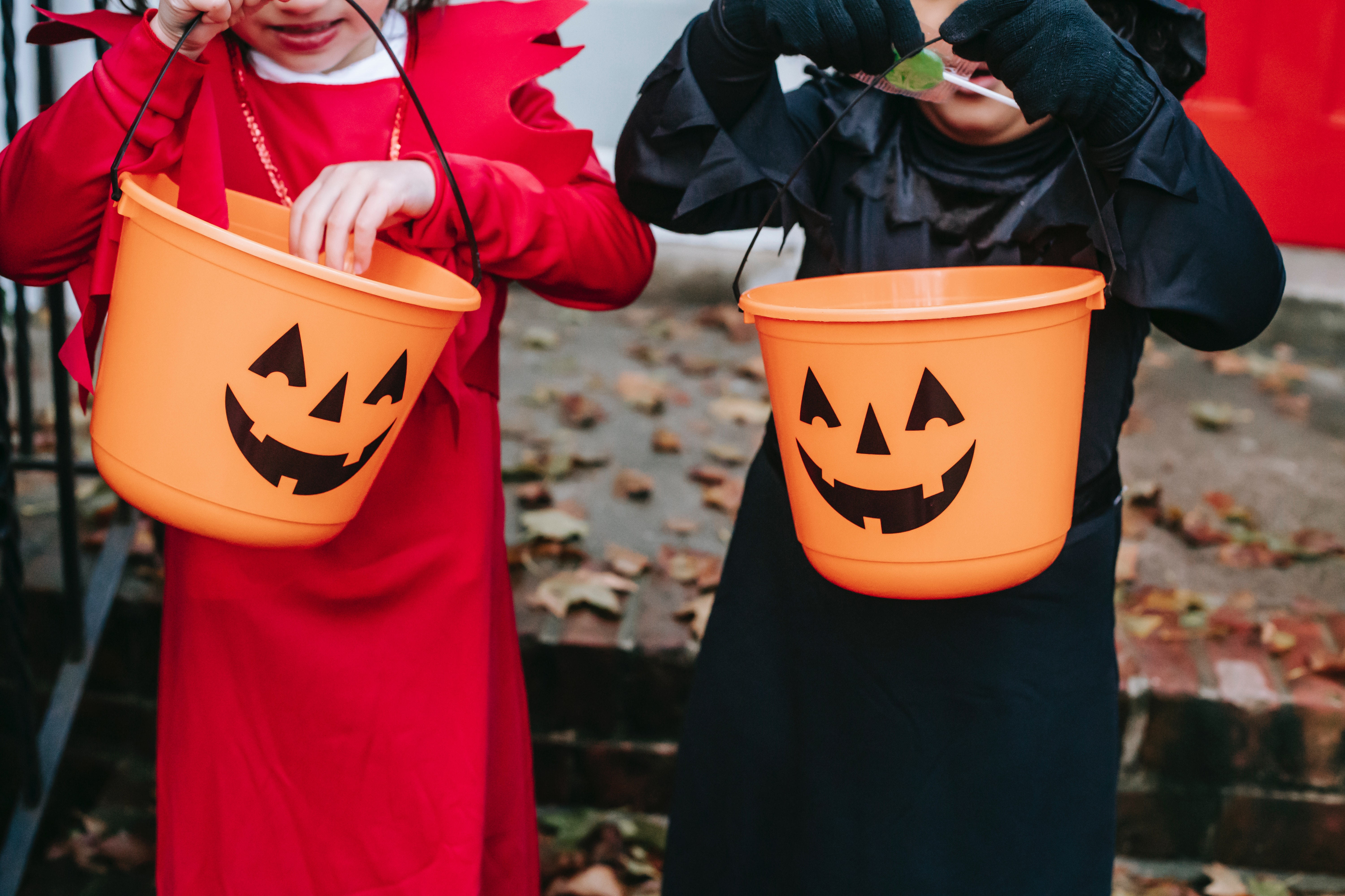 Close-up of two small, costumed children digging for candy in orange plastic totes.