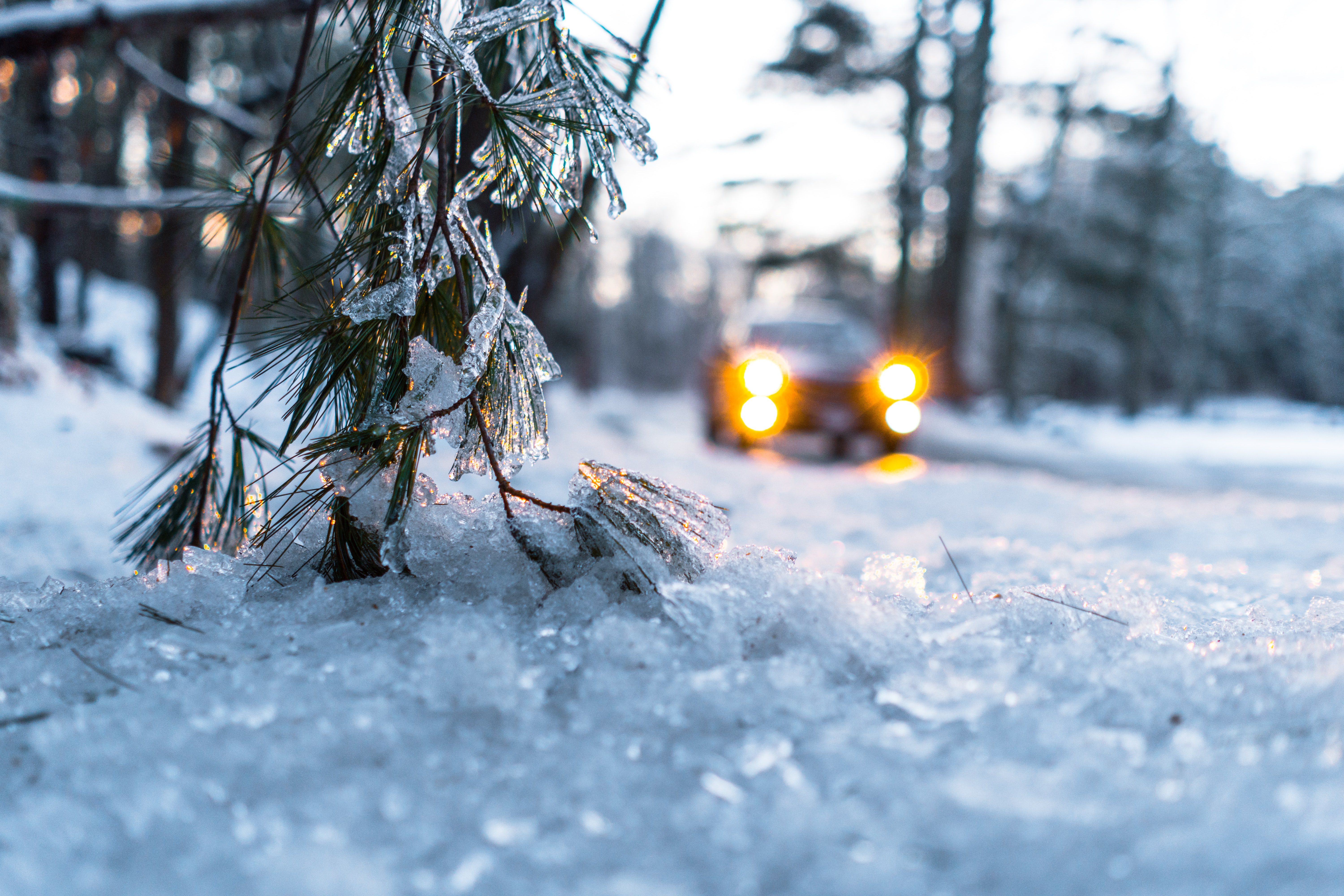 Close-up of icy winter road with car with head lights on visable in the background.