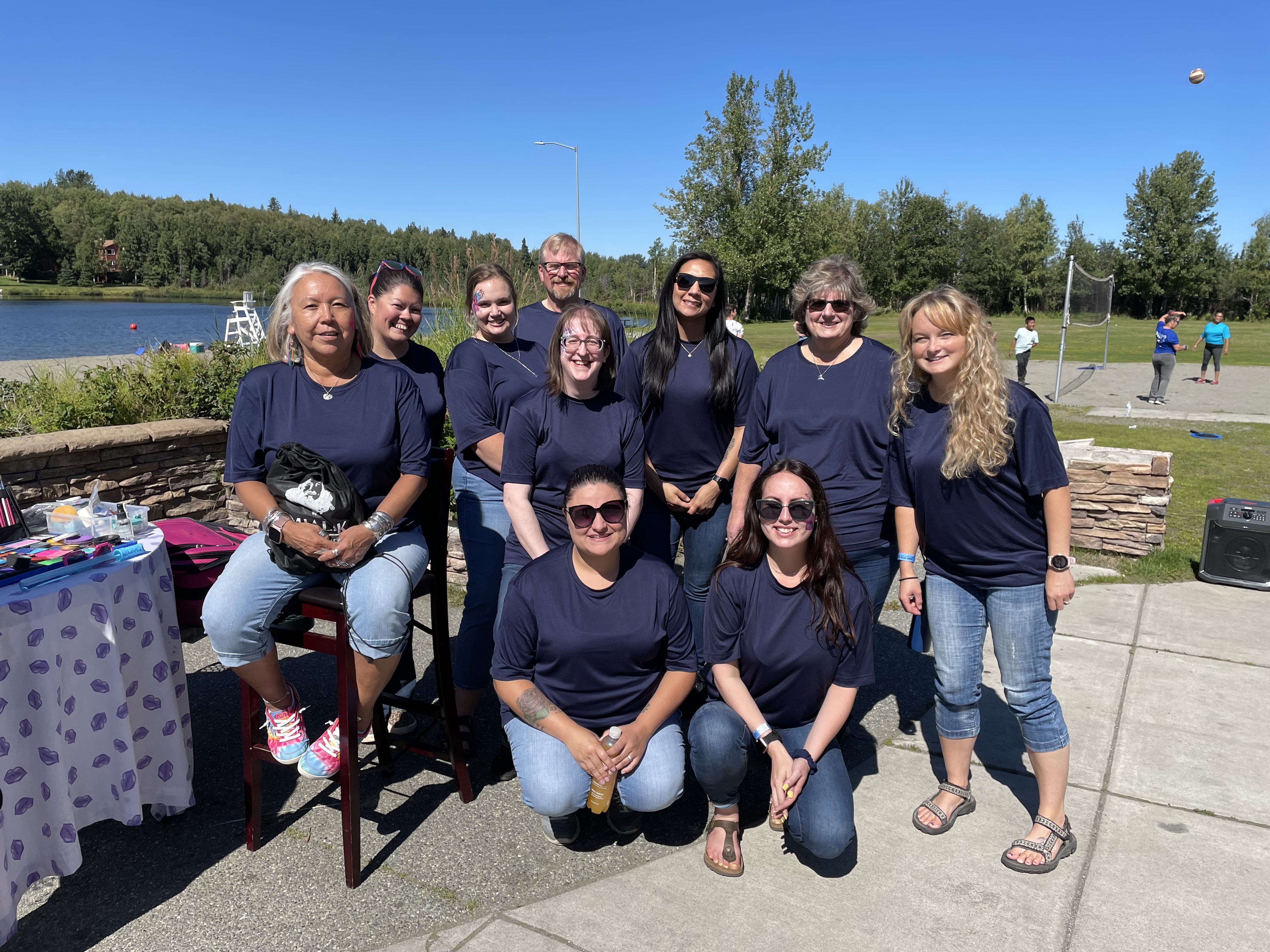 Group of Umialik employees in matching blue shirts posing together outdoors on a sunny day.