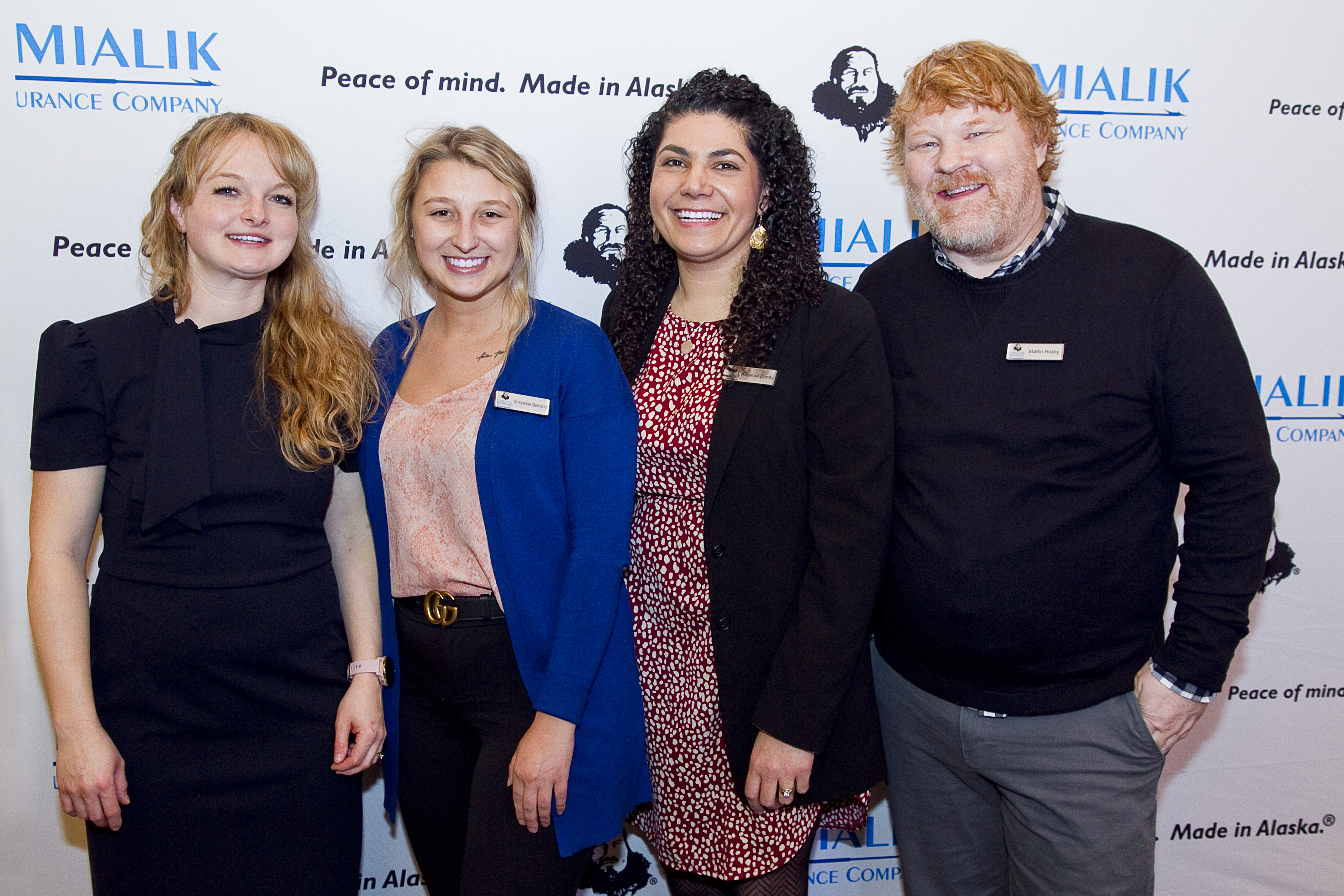 Four Umialik employees posing together in front of an Umialik-branded backdrop.