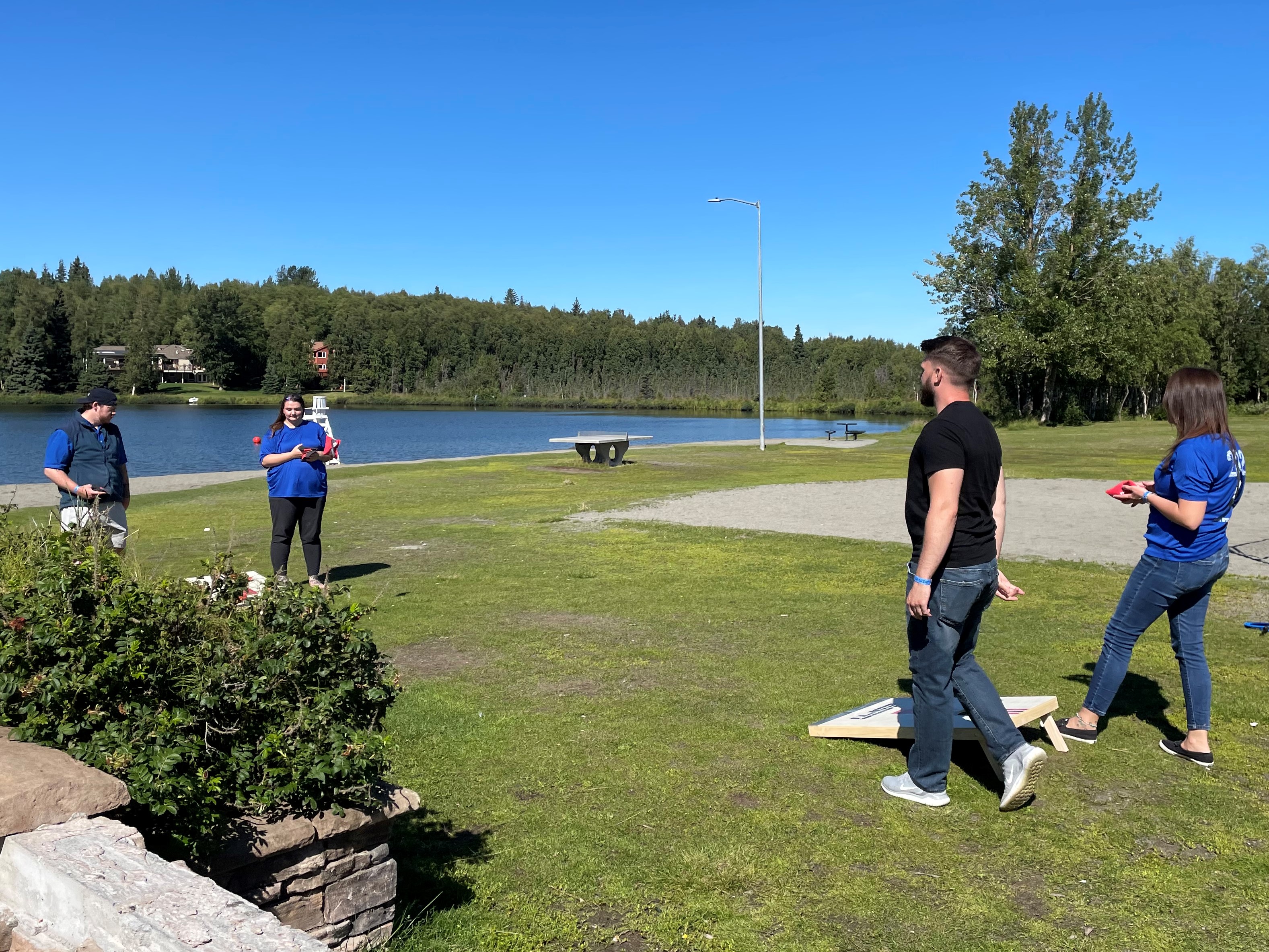 Four Umialik employees playing bean bag toss game outdoors on a sunny day.