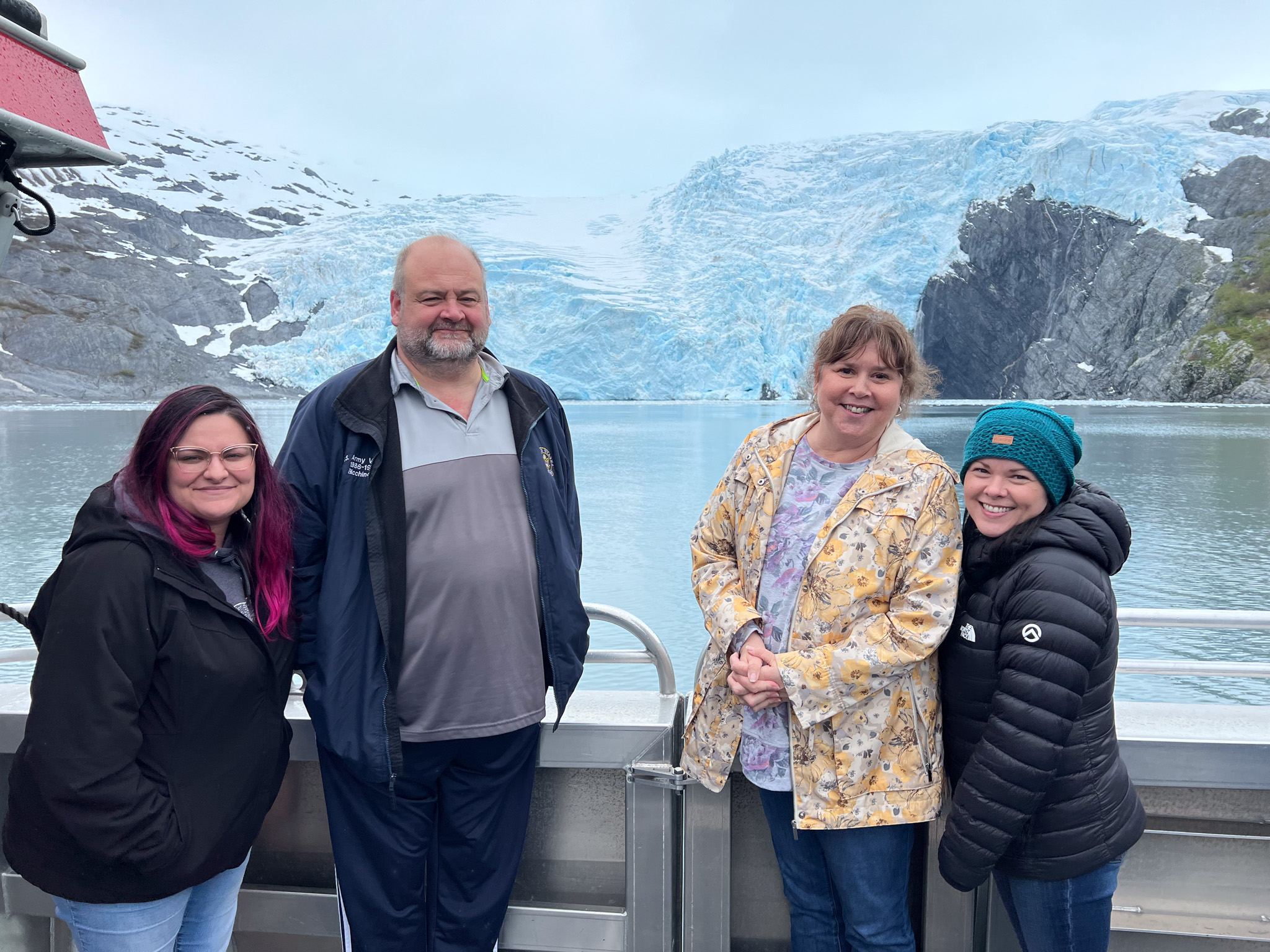 Four Umialik employees standing together on the deck of a large boat with glaciers in the background.