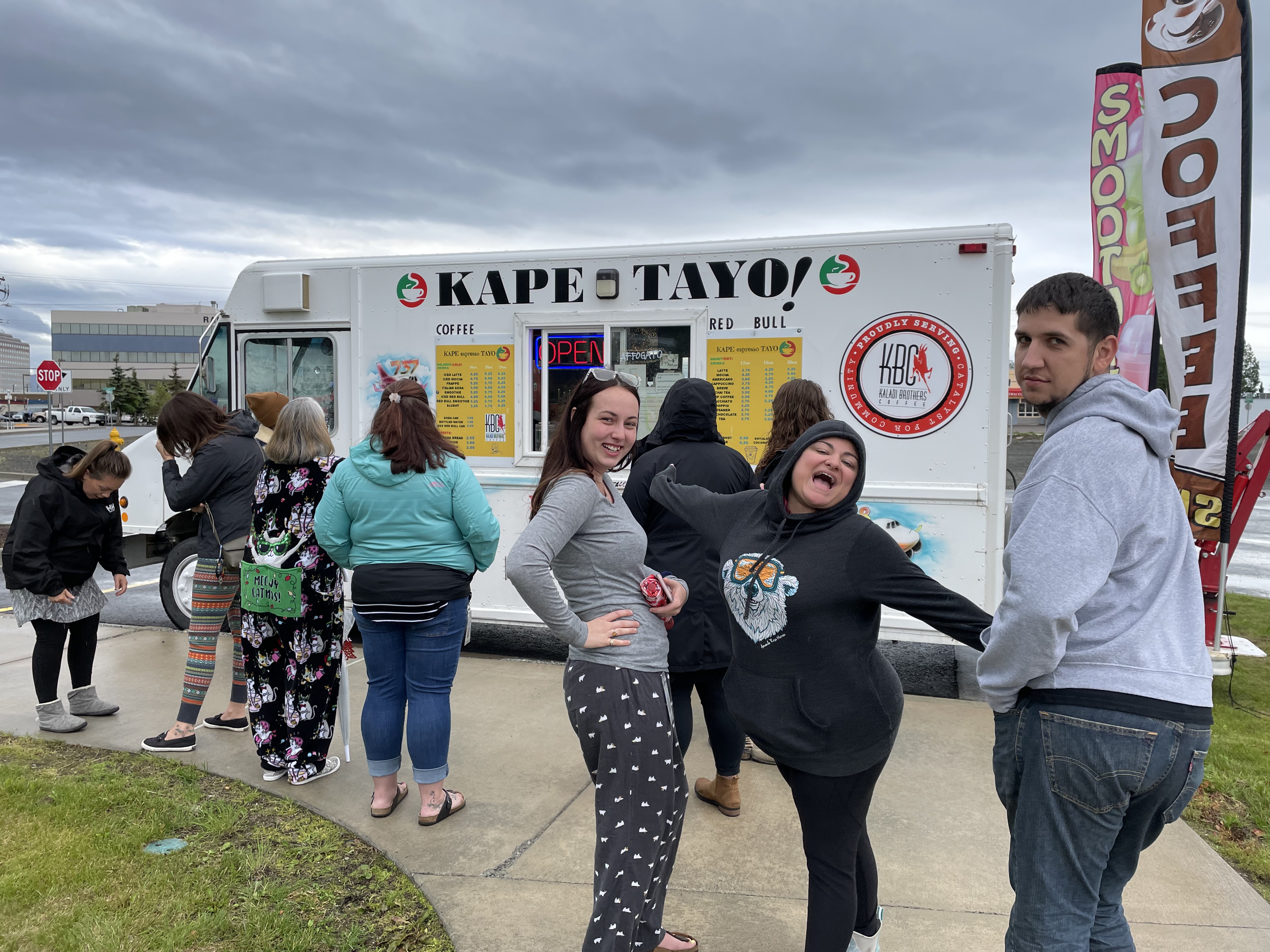 Group photo of three Umialik employees posing in front of a food truck and a line of other Umialik employees outdoors on a cloudy day.