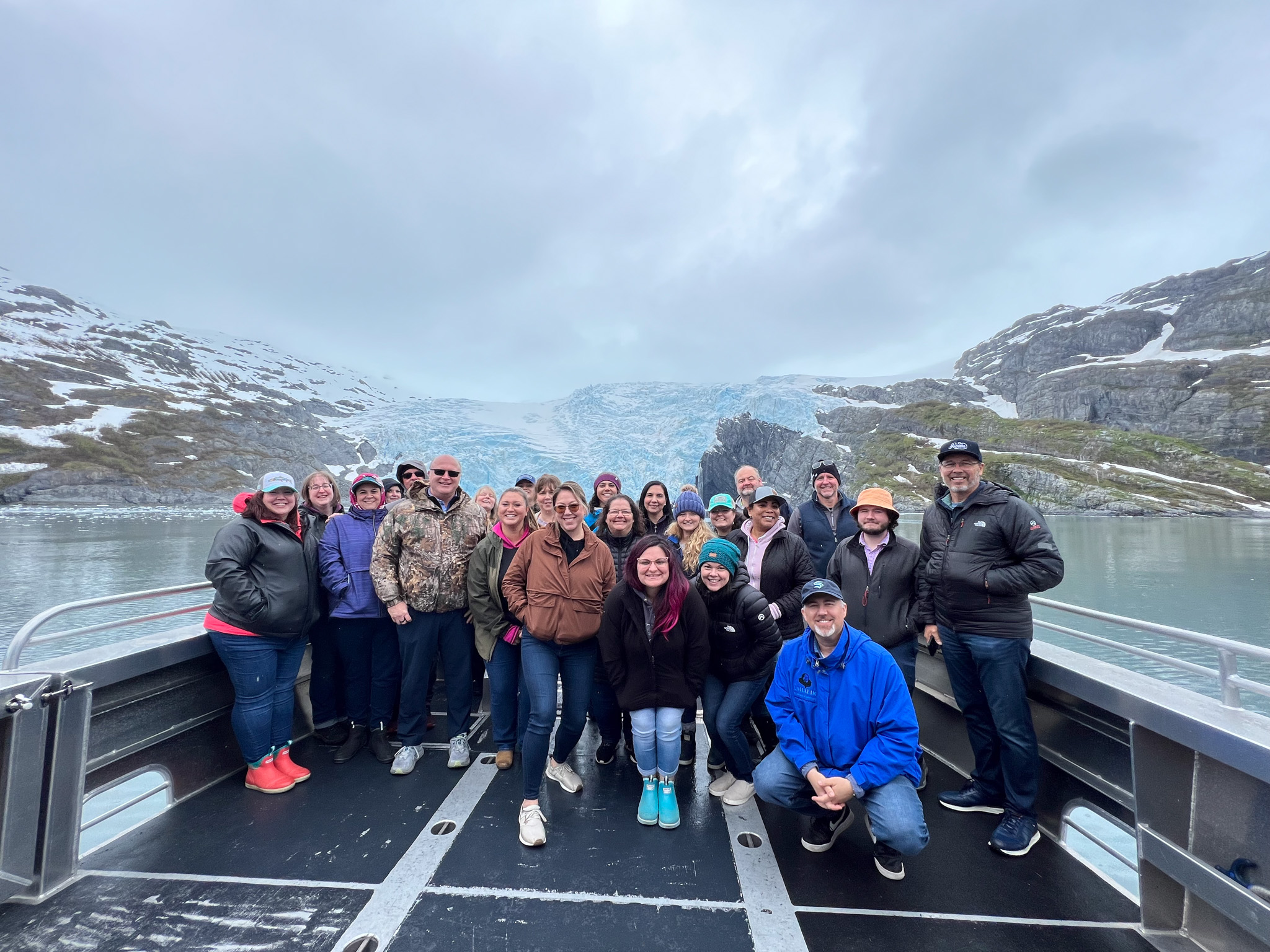 Group of Umialik employees standing together on the deck of a large boat with glaciers in the background.